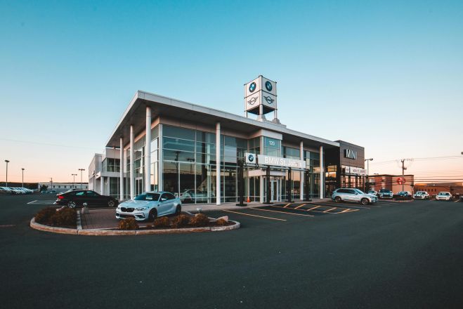 A modern BMW car dealership in a city with luxury cars and clear blue sky.