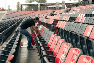 Workers preparing stadium seating for an upcoming sports event, organizing and cleaning rows of seats.